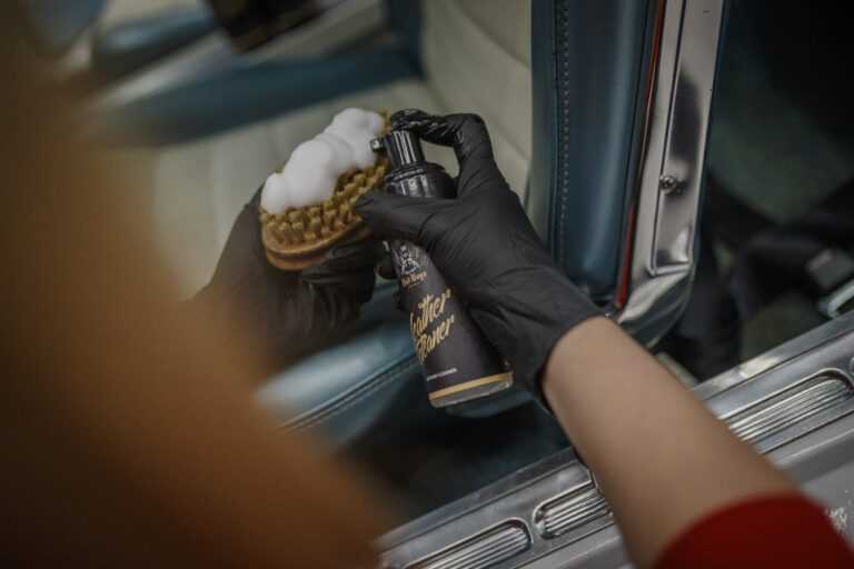 Leather Cleaner – Main gantée noire appliquant produit avec brosse ronde sur panneau cuir bleu clair voiture classique | Soin Cuir | miio Store