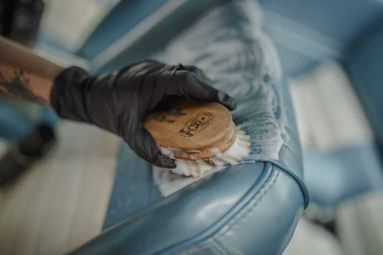 Leather Cleaner – Main gantée et brosse ronde nettoyant siège cuir crème vintage depuis perspective angulaire | Soin Cuir | miio Store